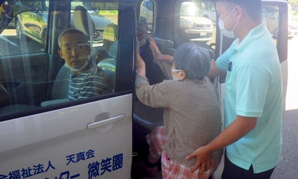 スタッフに支えられながらご利用者が送迎車に乗る写真