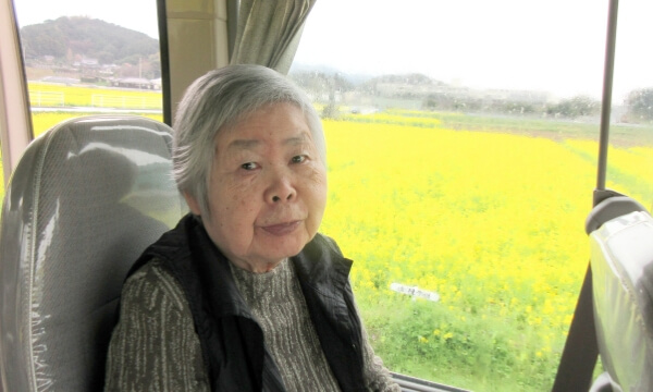 菜の花畑を背景にしたバス車内にいるご利用者の写真