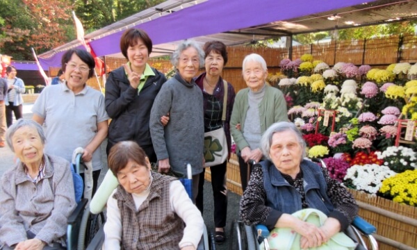 菊の前に並ぶ笑顔のご利用者とスタッフの写真